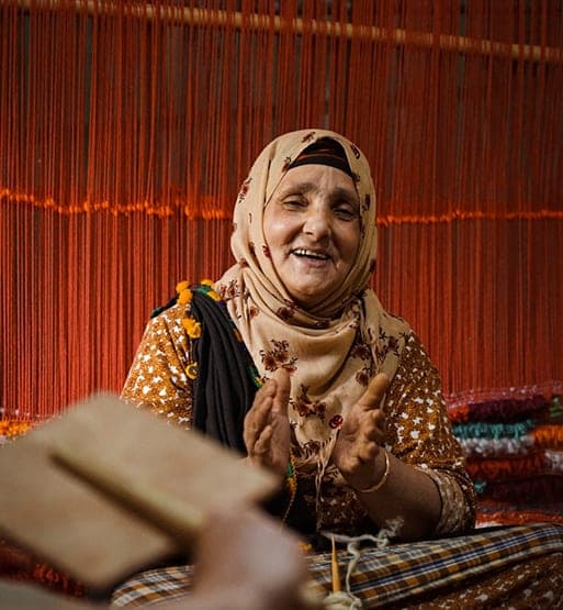 Artisane souriante travaillant devant des fils de tissage colores
